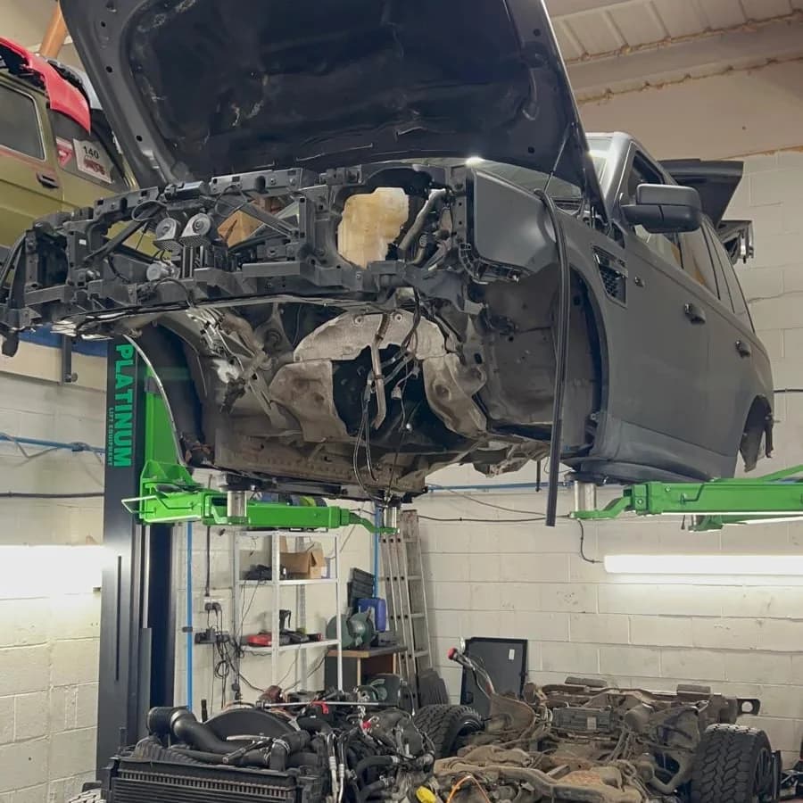 The body of a grey 4x4 raised on a two-post lift, with its chassis, engine and wheels on the floor beneath.