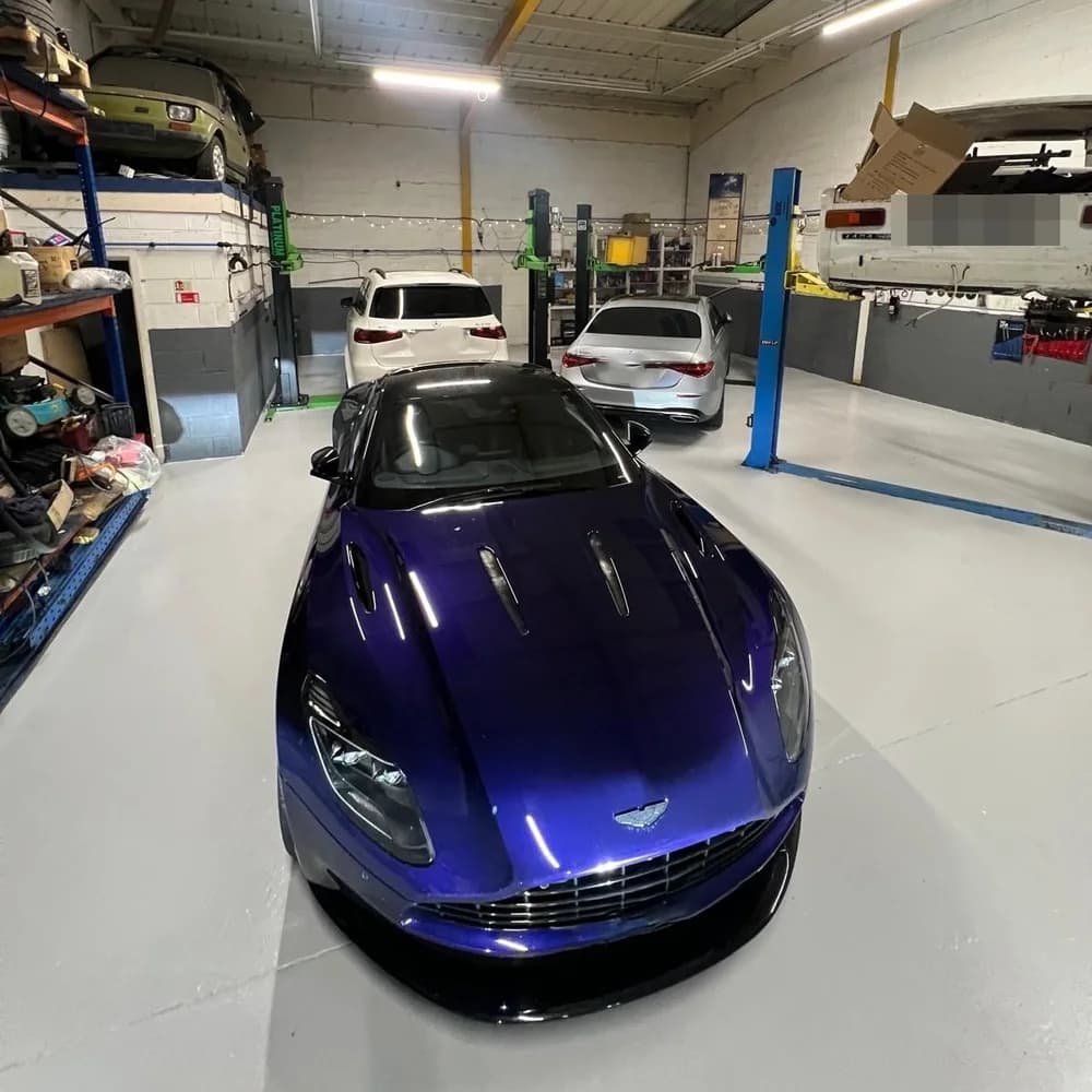 A blue Aston Martin in the workshop, with a white SUV, a silver saloon and a white Lada on a lift behind it.