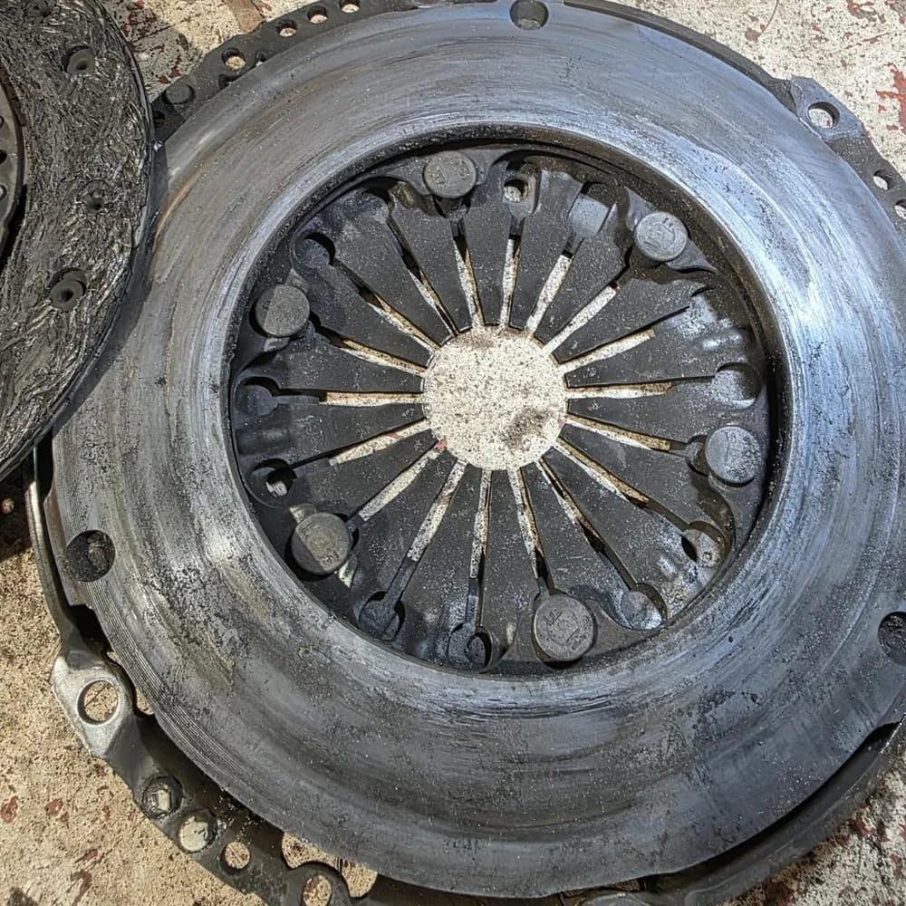 A used clutch pressure plate and friction disc laid out on the workshop floor.