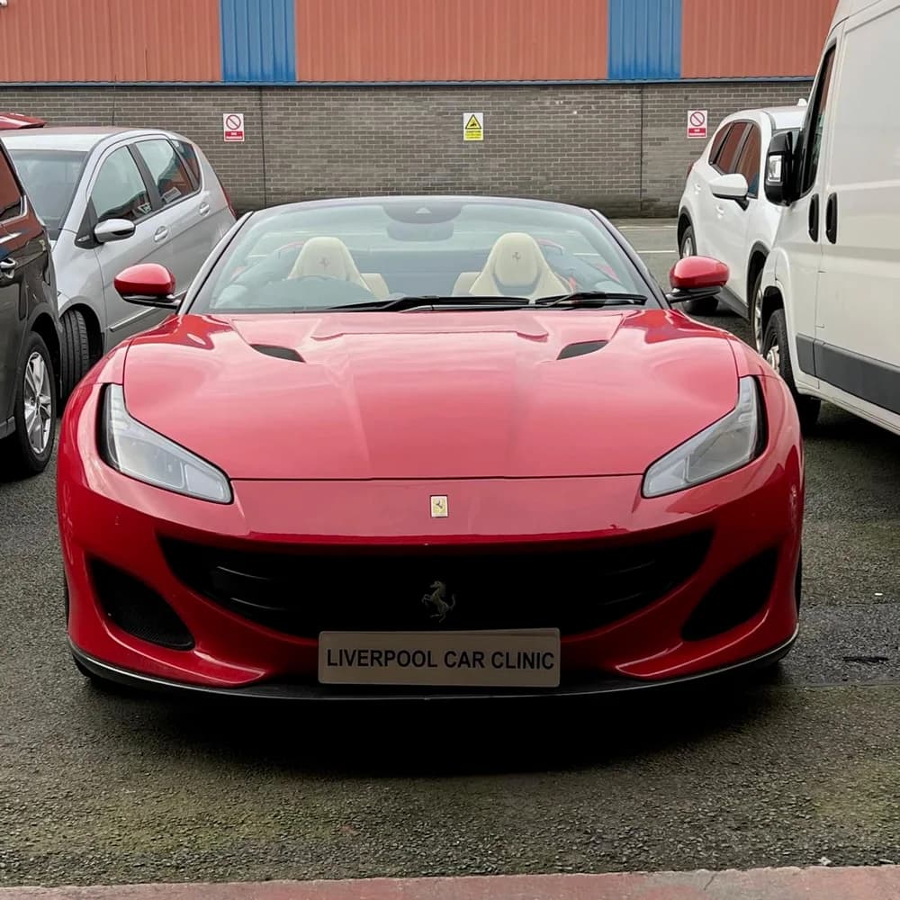 The front of a red Ferrari convertible with the roof down, carrying a Liverpool Car Clinic trade plate.