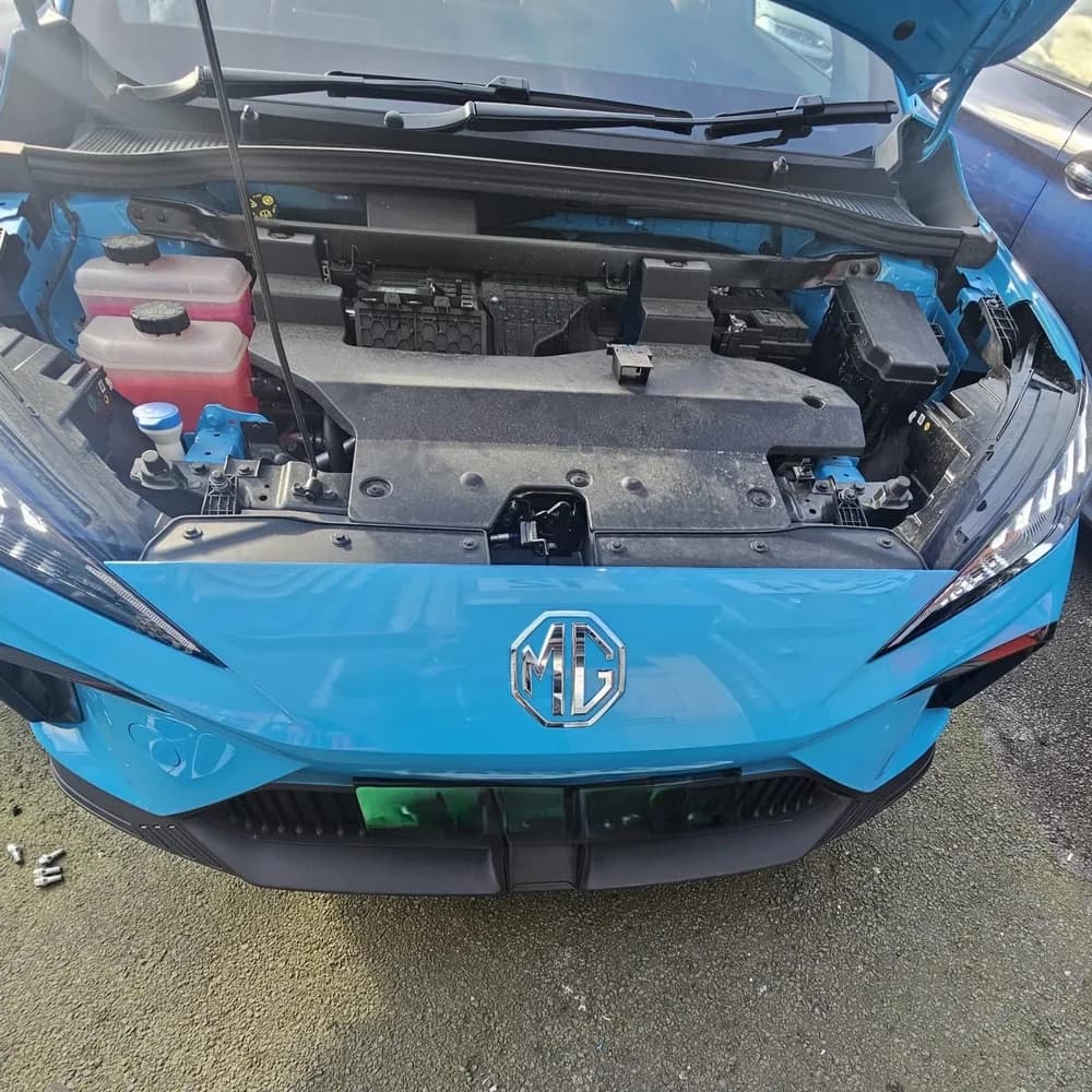 A blue MG with the bonnet up, parked outside on the tarmac.