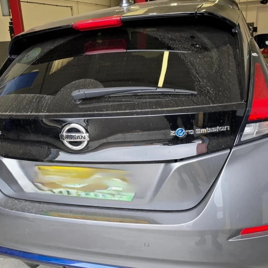 The rear of a grey Nissan Leaf in the workshop, with a technician crouched beside it.
