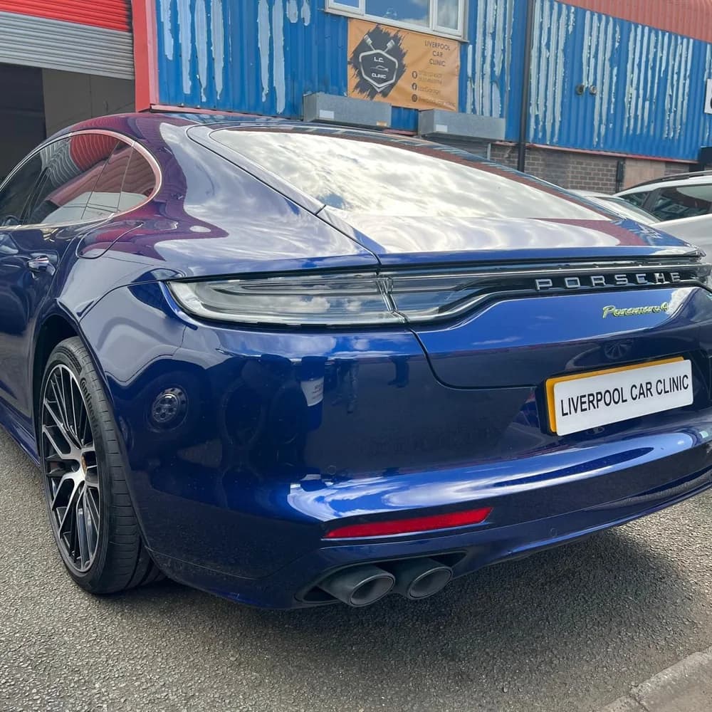 The rear of a blue Porsche Panamera 4 carrying a Liverpool Car Clinic trade plate, outside the workshop.