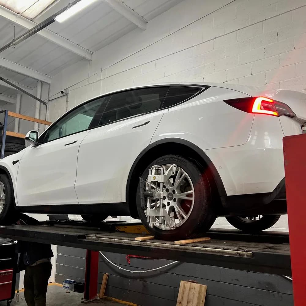 A white Tesla Model Y on a four-post ramp with wheel alignment clamps fitted.