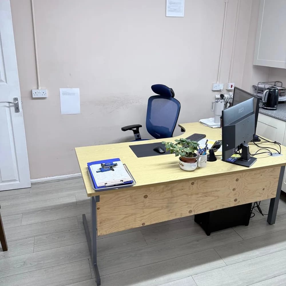 The office at the workshop, with a desk, a monitor and a mesh office chair.