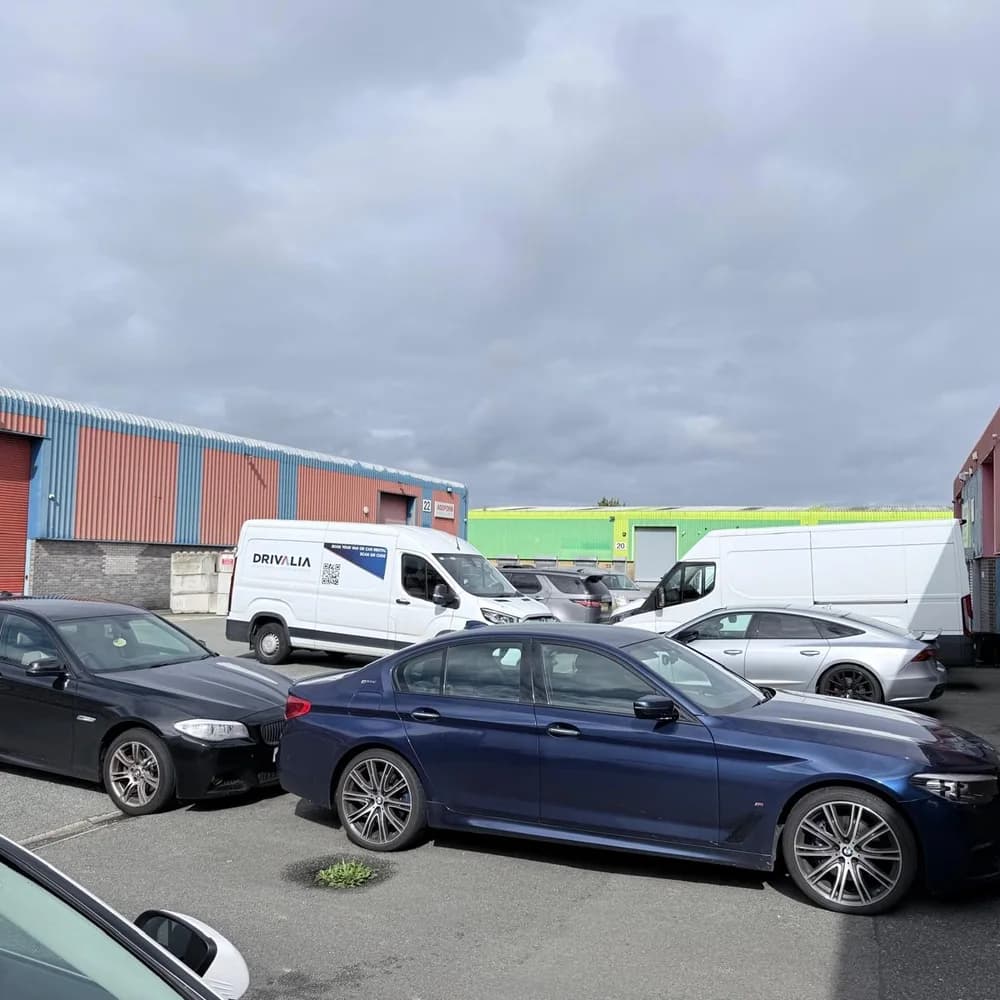 Cars and vans parked in the yard outside the units, with a Drivalia van behind two dark saloons.