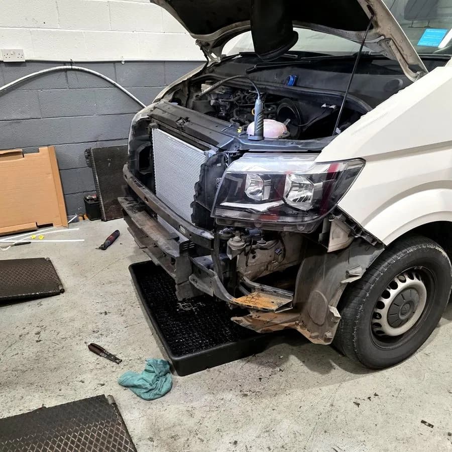 A Volkswagen Crafter van with the front bumper and grille removed, exposing the radiator pack during repair.