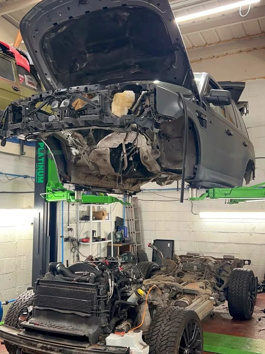 A Range Rover body raised on a two-post ramp with its engine and chassis assembly separated below.